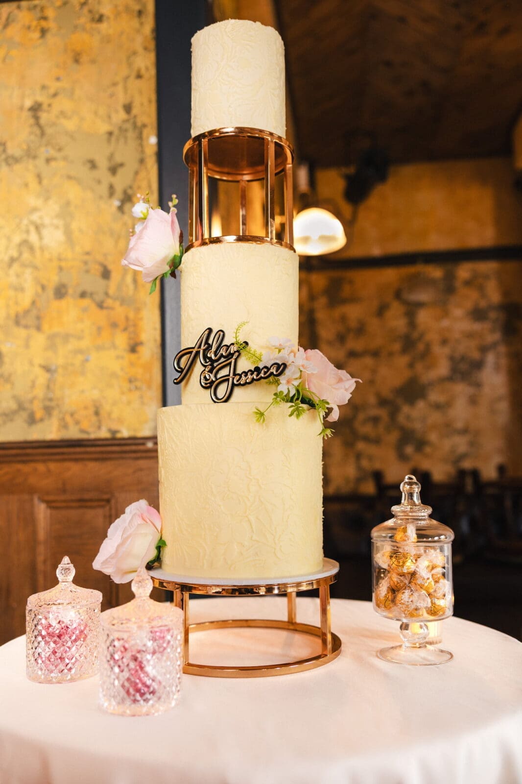 Three tier ivory wedding cake with gold topper and candy jars by Wee Cupcakes during Black Romance London editorial at Prince of Peckham