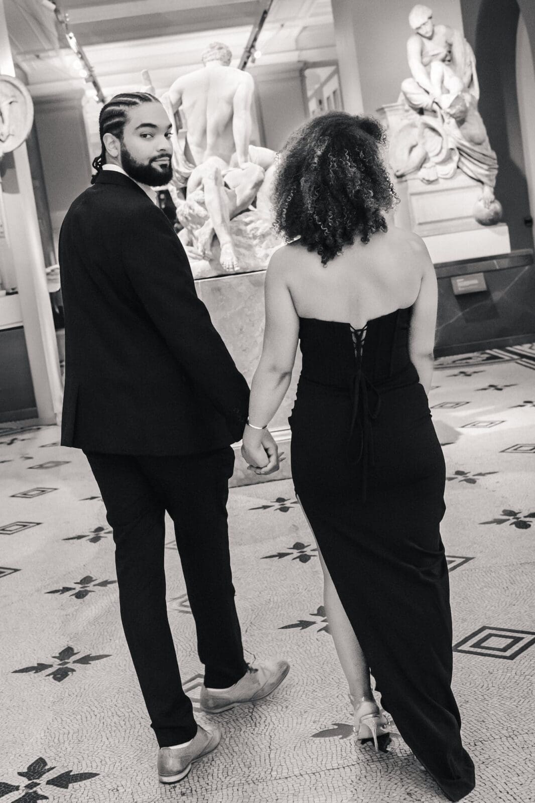 Romantic portrait of couple walking through gallery at Victoria and Albert Museum during London engagement shoot