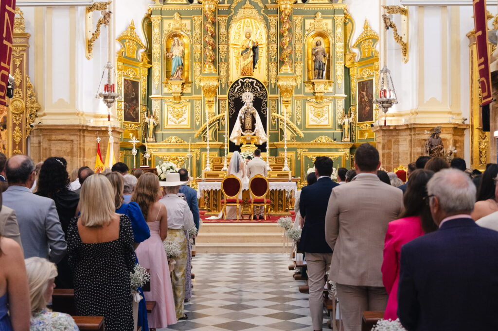 Wide view of Anna and Michael standing at the altar during their wedding ceremony at Iglesia de la Encarnación in Marbella, with guests standing throughout the cathedral.