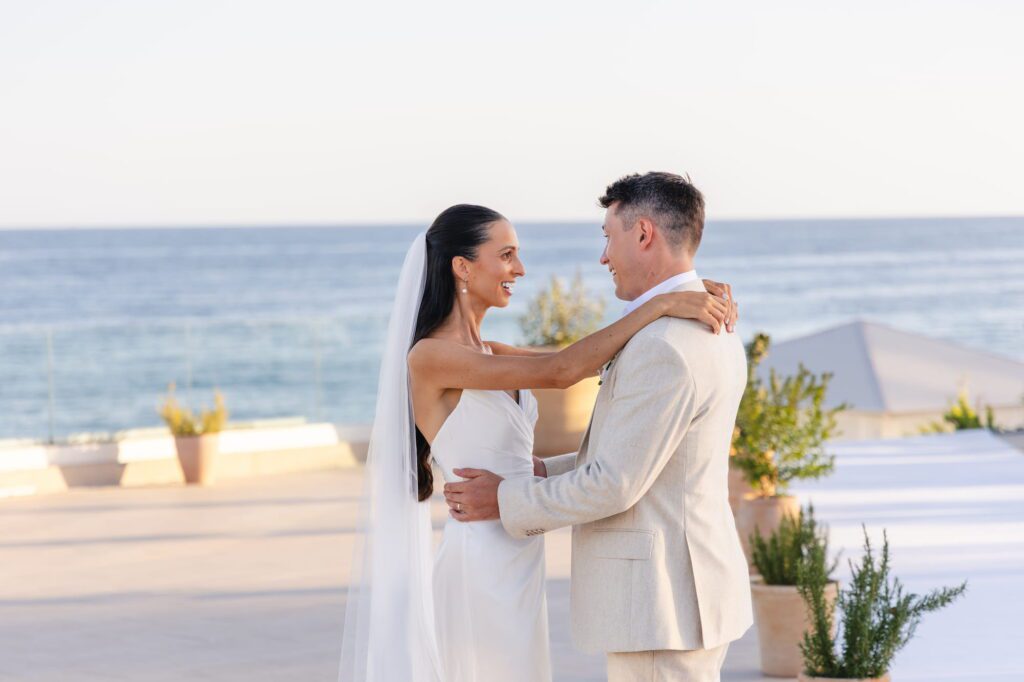 Anna and Michael embracing and looking into each other's eyes with the ocean behind them